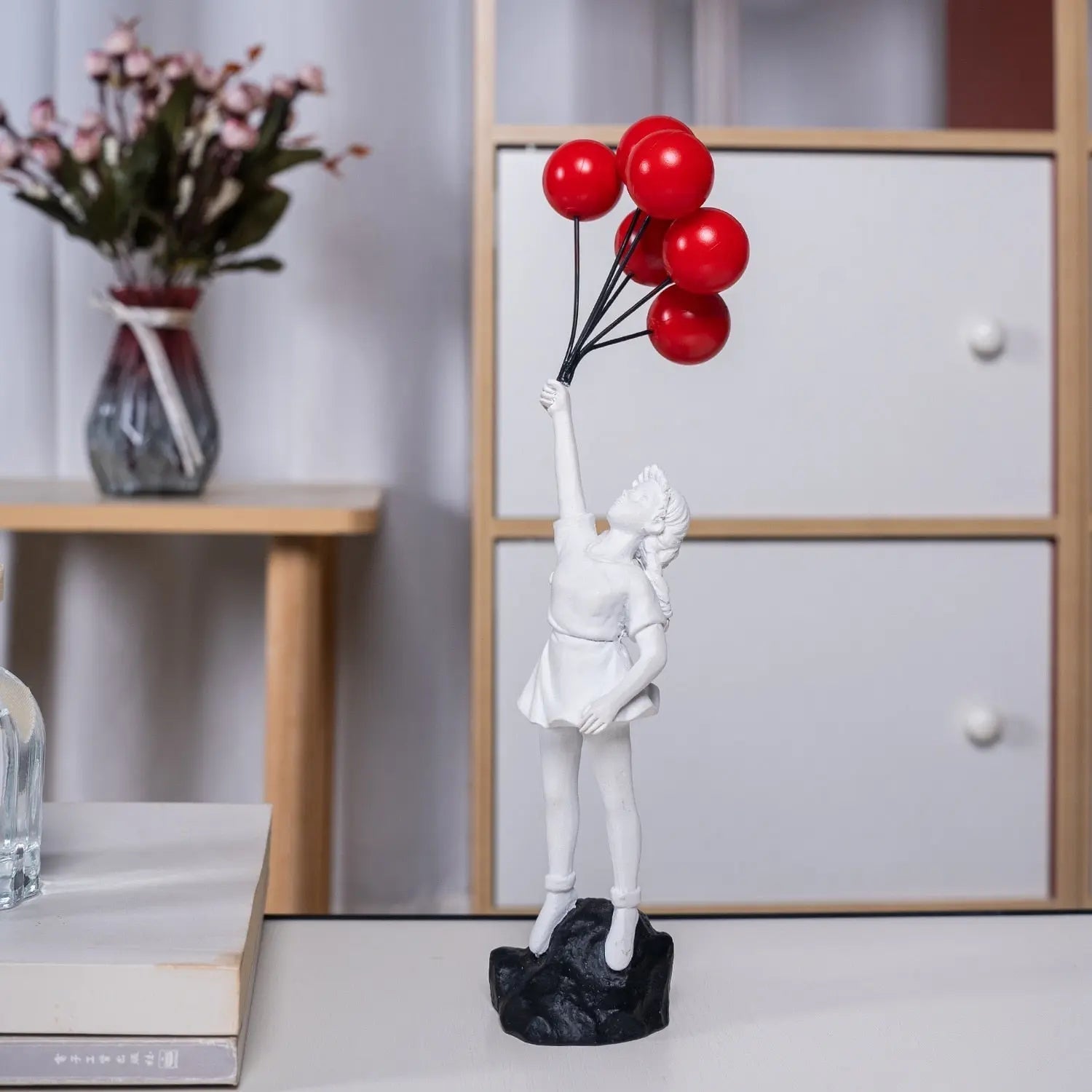 White figurine holding red balloons on a black base in a room setting.