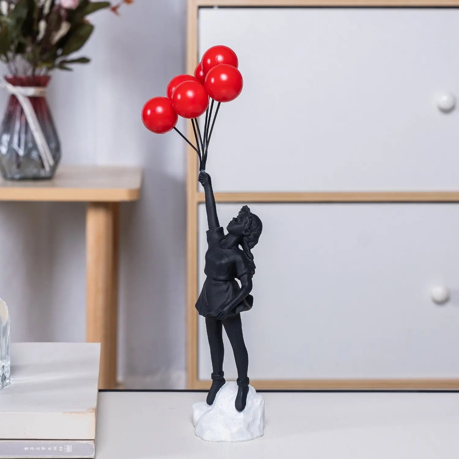 Black figurine holding red balloons on a white base in a room setting.